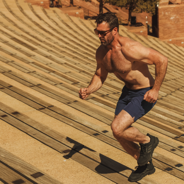 Shirtless runner in navy Shinesty athletic shorts charging up wooden amphitheater steps
