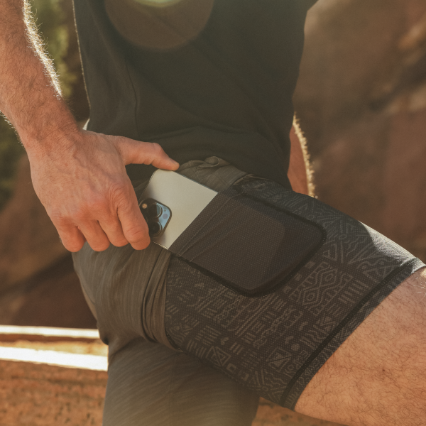 Hand sliding a phone into the thigh pocket of a gray patterned liner beneath black athletic shorts
