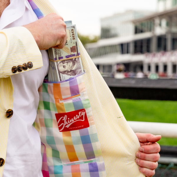 Pale yellow Shinesty party blazer held open, plaid lining and a stack of cash in the inside pocket, racetrack behind