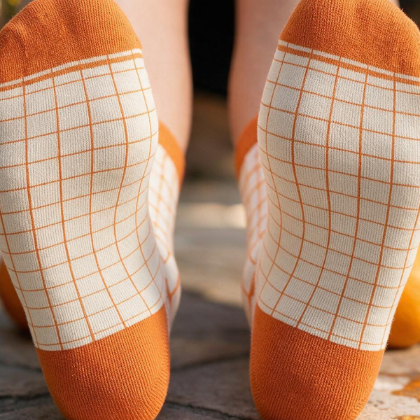 Soles of orange-and-cream windowpane Shinesty quarter socks, kneeling on stone pavers