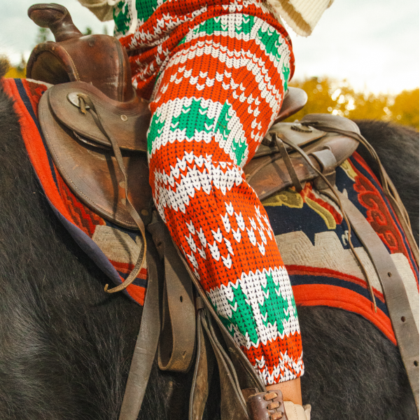 Leg of holiday fair-isle women's pajamaralls tapering to the ankle, seated in a leather saddle on a shaggy black yak